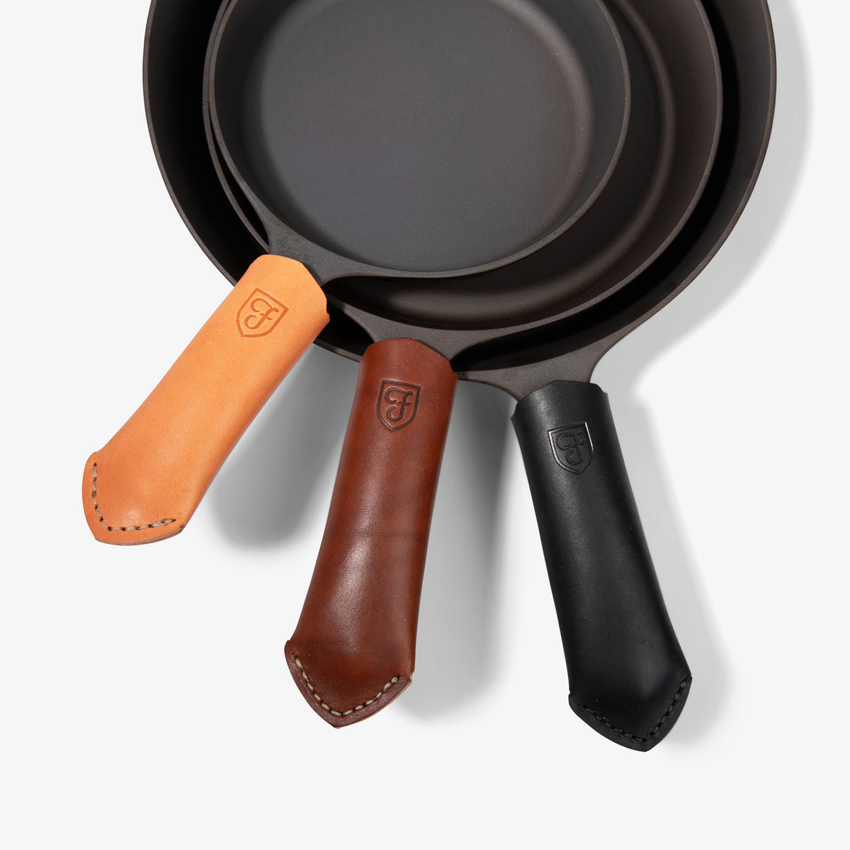 Cognac, brown and black Field leather handle covers on three cast iron skillet handles