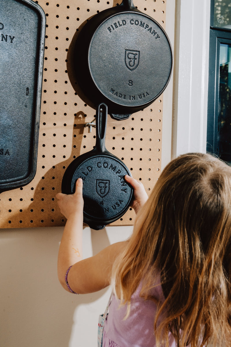 A child hanging a No.8 Field Skillet on a kitchen pegboard